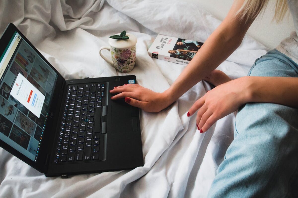 À propos A person uses a laptop while resting on a bed, depicting a cozy work-from-home setup.